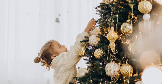 little girl reaching up to put an ornament on a christmas tree