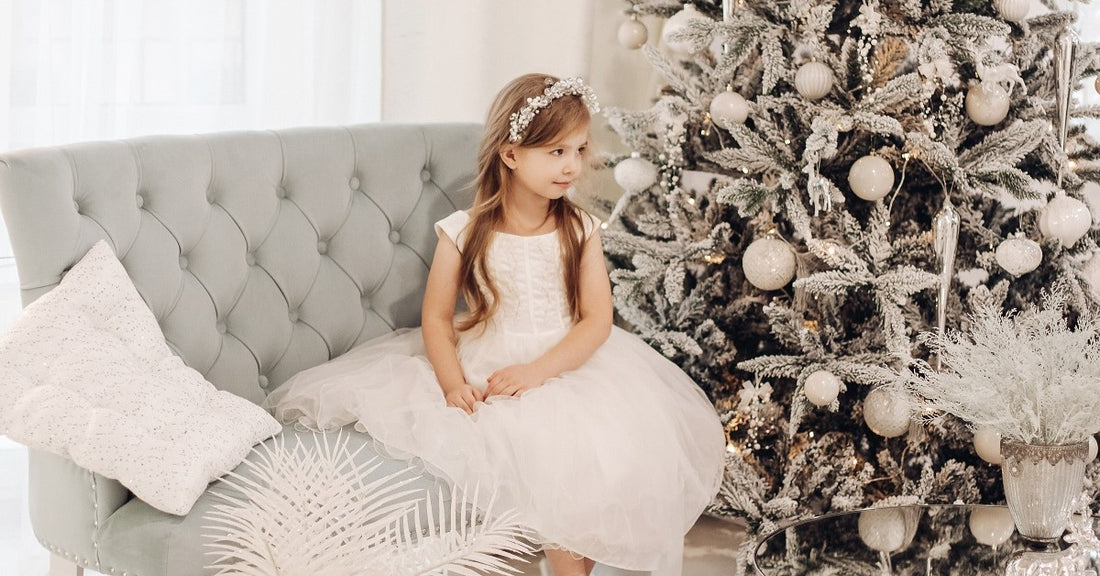 Little kid dressed as a princess on a sofa next to a Christmas tree with toy icicles and balls.